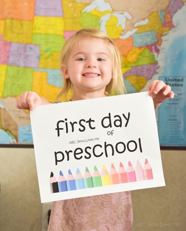 Preschool girl hold a "first day of ABCJesusLovesMe preschool"  sign.