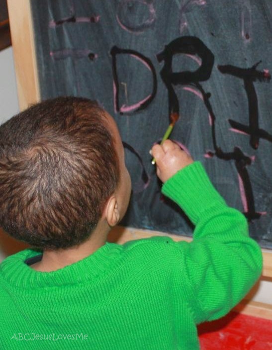 Preschooler creating letter with paintbrush.