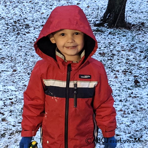 A preschool boy standing in the snow.