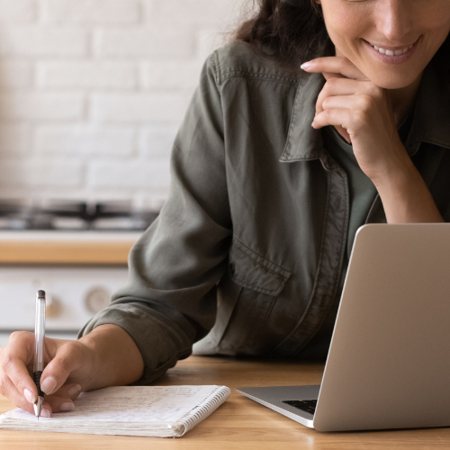 A woman on a laptop, taking notes for video demo.